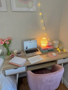 a laptop computer sitting on top of a wooden desk next to a pink chair and lamp