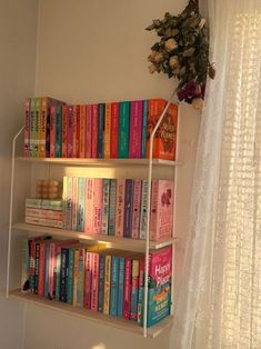 a book shelf filled with lots of books next to a white curtain and window sill