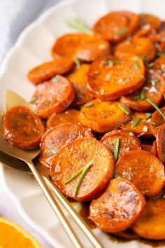 a white plate topped with sliced up carrots next to silverware and an orange slice