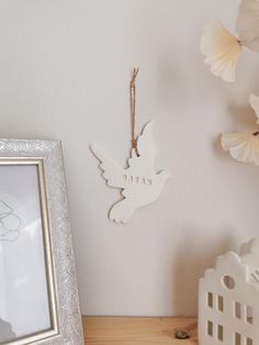 a white bird ornament hanging on a wall next to a framed photo and flowers