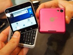 a person holding a pink cell phone next to a pink and silver smart phone on top of a table