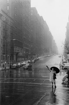 a woman is holding an umbrella in the rain on a city street with cars and buildings