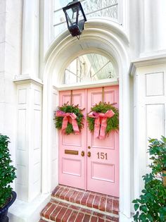 two wreaths are hanging on the front door of a pink house with red brick steps