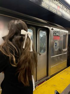 a woman with a bow on her head standing in front of a train at the station