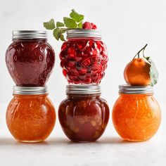 four jars filled with different types of jams and fruit sitting on top of each other