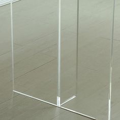 an empty glass table on the floor in front of a white wall and wooden floors