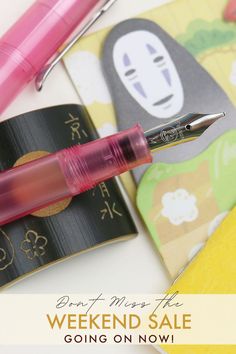 a pink pen sitting on top of a notebook next to a notepad and pens