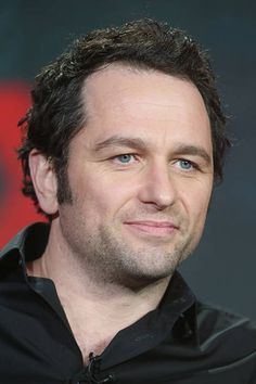 a close up of a person wearing a black shirt and looking at the camera with a smile on his face