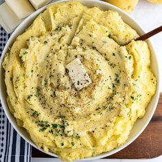 a bowl filled with mashed potatoes topped with butter and seasoning next to sliced lemons