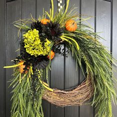 a wreath is hanging on the door with flowers and greenery in front of it