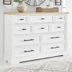 a white dresser with lots of drawers and a clock on the wall in the background