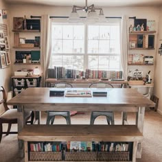 a dining room table with two benches in front of it and bookshelves on the wall