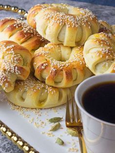 a white plate topped with rolls covered in sesame seeds next to a cup of coffee