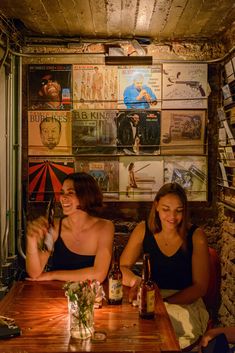 two women sitting at a wooden table in front of posters on the wall behind them