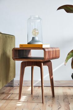 a wooden table with a glass jar on top of it next to a plant and a couch