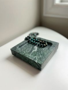 a wooden box with beads on it sitting on top of a white table next to a window