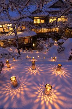 many candles are lit in the snow near a building with windows and lights on it