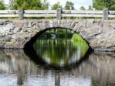 a stone bridge over a body of water with a boat in the distance under it