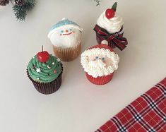 three cupcakes with frosting and decorations on them sitting next to a christmas tree