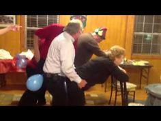 two men and one woman are dancing in a living room with balloons on the floor