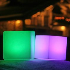 two illuminated cubes sitting on top of snow covered ground in front of a building