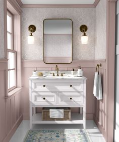 a bathroom with pink walls and white vanity, gold mirror over the sink, and rug on the floor