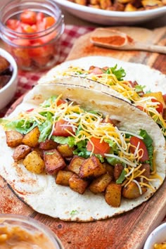 two tacos are sitting on a cutting board next to bowls of salsa and tortillas