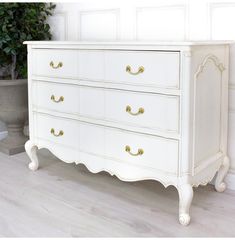 an antique white dresser with gold handles in a living room or dining room, next to a potted plant