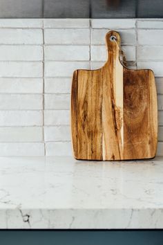 a wooden cutting board sitting on top of a white tiled counter next to a brick wall