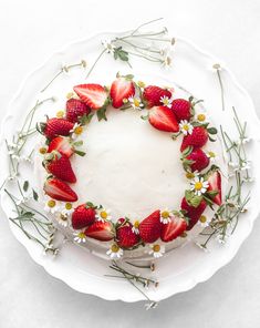 a cake decorated with strawberries and daisies on a white plate in the shape of a wreath