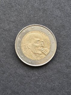 a close up of a coin on a gray surface with the image of a man's face