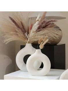 two white vases sitting on top of a table filled with dry grass and feathers