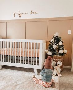 a baby is sitting on the floor in front of a crib next to a christmas tree