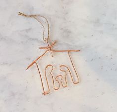 a house shaped ornament hanging from a string on a marble surface with copper wire