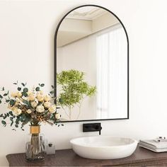 a white sink sitting under a large mirror next to a vase with flowers in it