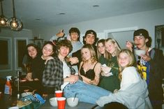 a group of young people posing for a photo in a living room with drinks and food