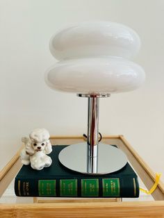 a small white dog figurine sitting on top of a book with a lamp in the background