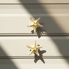 two gold starfishs sitting on the side of a white wall next to each other