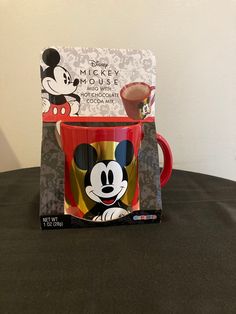 a mickey mouse coffee cup and saucer sitting on a table with a card in front of it