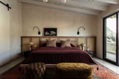 a bedroom with a large bed and an ottoman in front of a sliding glass door