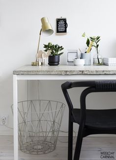 a white desk topped with a black chair next to a table covered in potted plants