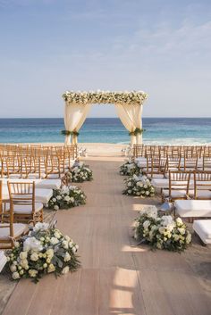 an outdoor ceremony set up on the beach with white flowers and greenery in front of the ocean