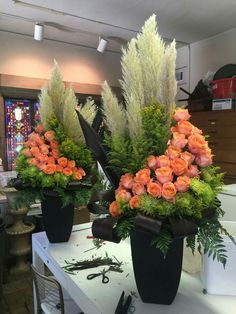 two black vases filled with orange flowers on top of a white table in a room