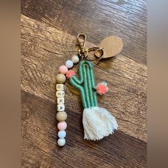 a keychain with a cactus charm and tassels attached to it on a wooden table