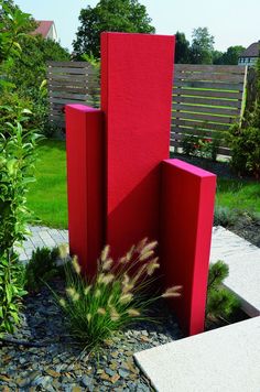 a tall red sculpture sitting in the middle of a garden next to a brick walkway