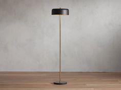 a floor lamp with a black shade on the top and a gold base, standing on a wooden floor