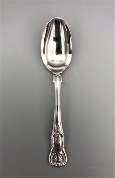 a silver spoon with an ornate design on the top and bottom, sitting against a gray background