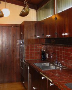 a kitchen with wooden cabinets and red tile backsplash, two hanging pots above the sink