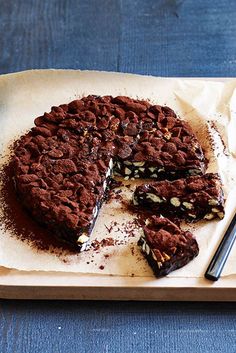 a chocolate cake with one slice cut out on a wooden cutting board next to a knife and fork