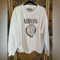 a white sweater with the words nirvana on it hanging from a wicker chair in front of a wall